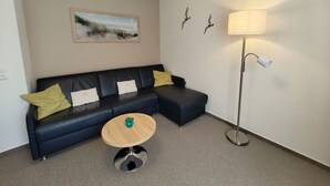 A modern living room with a dark blue sectional sofa, a round wooden coffee table, and a floor lamp. - Apartment 5, 2- room, 50 m², mezzanine floor, garden use - guest house Müller (Scharbeutz)