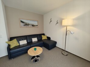 A modern living room with a dark blue sectional sofa, a round wooden coffee table, and a floor lamp.