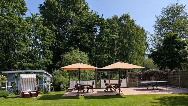 A backyard with a covered patio area, a small glass structure, and a tennis table. - Apartment 5, 2- room, 50 m², mezzanine floor, garden use - guest house Müller (Scharbeutz)
