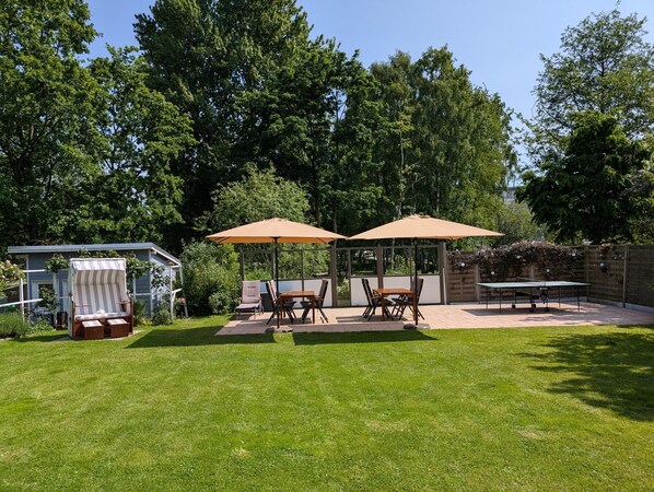 A backyard with a covered patio area, a small glass structure, and a tennis table.