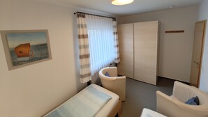 A hotel room with a bed, a chair, a wardrobe, and a painting on the wall. - Apartment 5, 2- room, 50 m², mezzanine floor, garden use - guest house Müller (Scharbeutz)