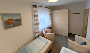 A hotel room with a bed, a chair, a wardrobe, and a painting on the wall.