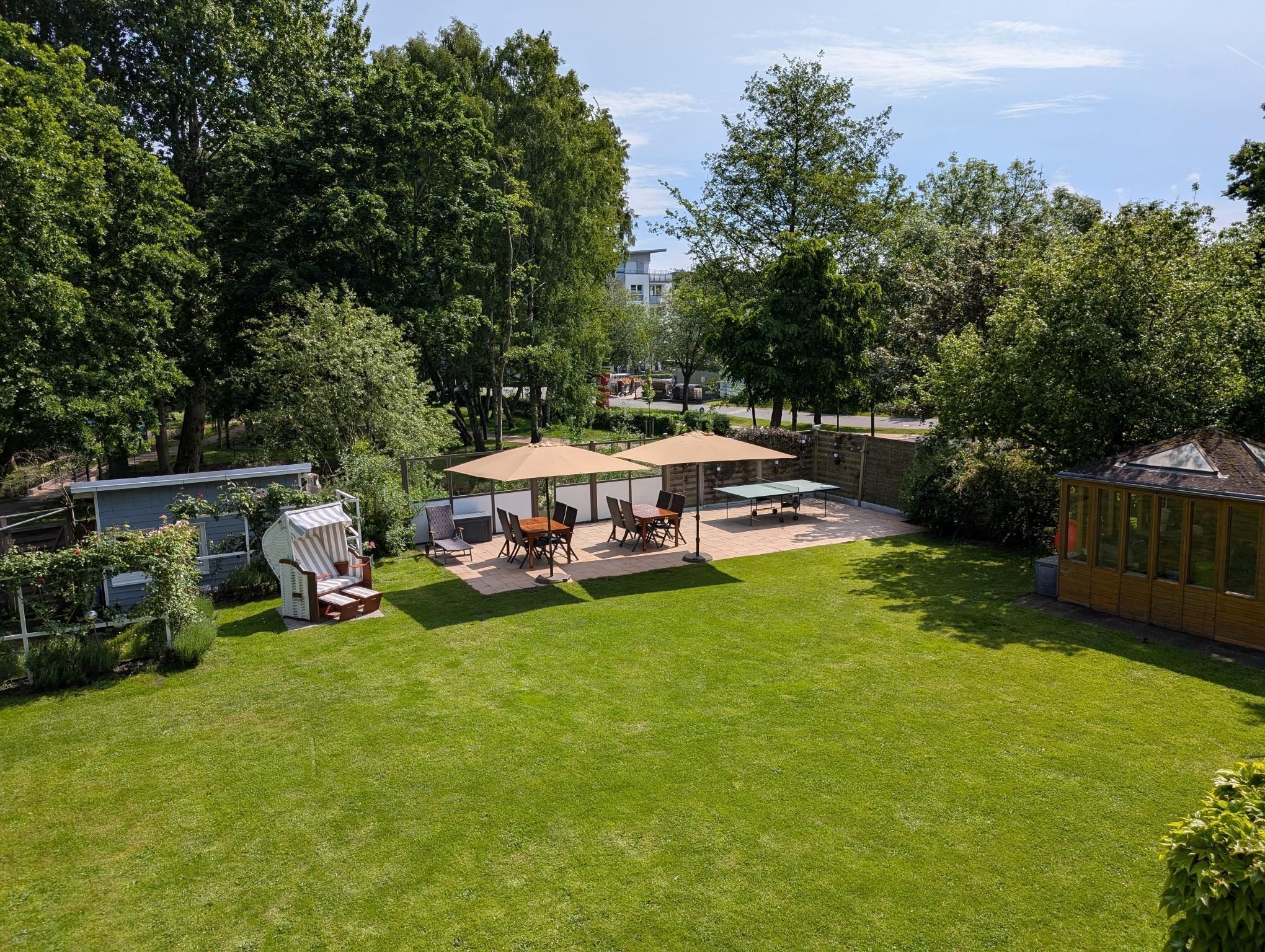 Een goed onderhouden terras met een tafel en stoelen, omringd door weelderige beplanting en bomen.