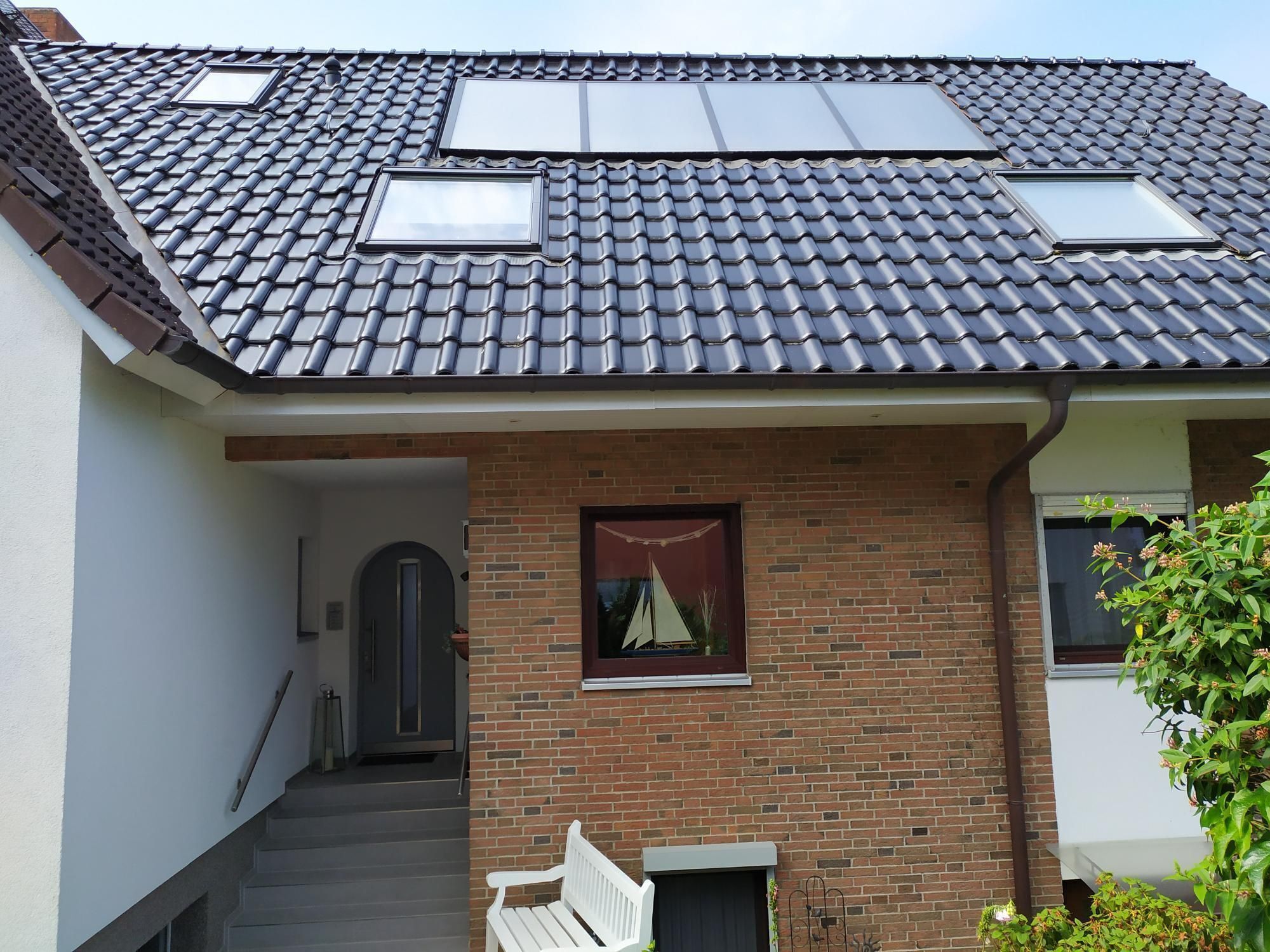 A two-story house with a tiled roof, a brick facade, and a small porch with a bench.
