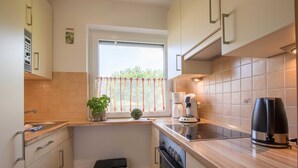 A compact kitchen with a window, a coffee maker, and a trash bin. - Apartment 5, 2- room, 50 m², mezzanine floor, garden use - guest house Müller (Scharbeutz)