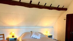Een gezellige slaapkamer met een houten plafond, een enkel bed met een witte quilt, twee nachtkastjes met lampen, en een houten stoel.