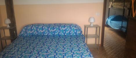 Een slaapkamer met een bed met een decoratieve spreidek, twee bedlampen, een stapelbed met een blauwe deken en een betegelde vloer.