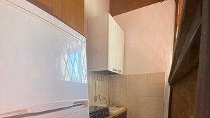 A compact kitchen with wooden cabinets, a white refrigerator, and a tiled backsplash. - Michelangelo House, bilo (Gioiosa Marea)