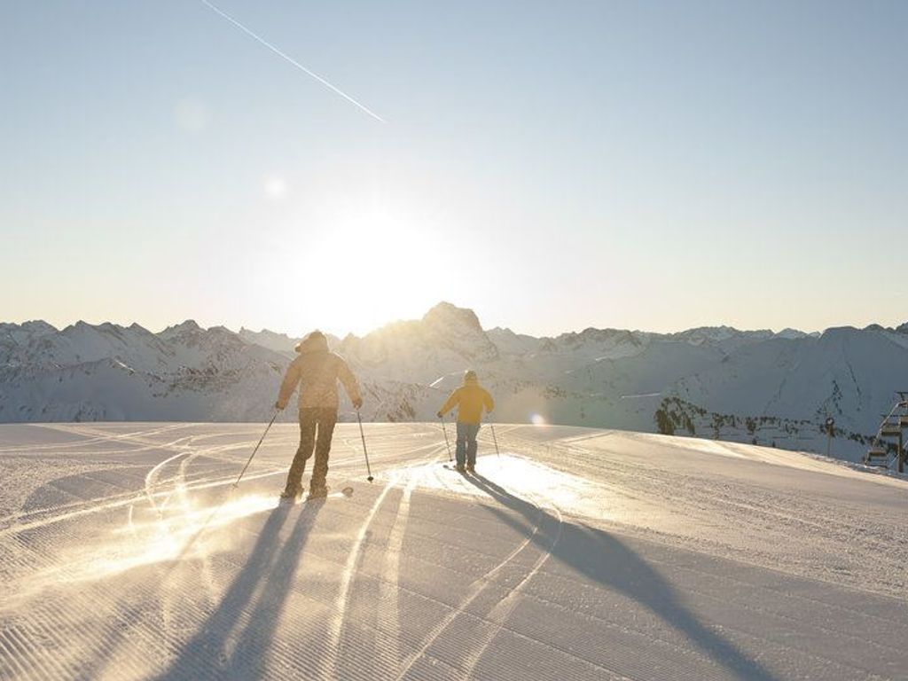 Due sciatori su una pista innevata con montagne sullo sfondo.