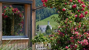 Ein Holzhaus mit einem Fenster, das auf eine grüne Landschaft und eine Kirche blickt.