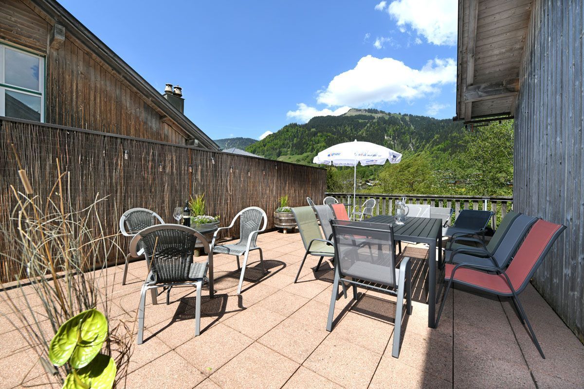 An outdoor patio with a table and chairs, a wooden fence, and a view of green hills.