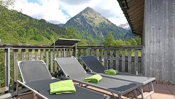 Ein Balkon mit zwei Liegestühlen, einem Holzzaun und Blick auf die Berge.
