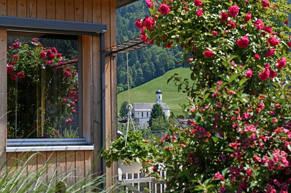 Ein Holzhaus mit einem Fenster, das auf eine grüne Landschaft und eine Kirche blickt.