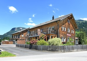 A wooden building with balconies, a sign indicating it's a guesthouse, and a mountain in the background.