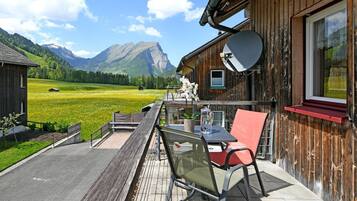 A wooden cabin with a balcony overlooking a green field and mountains.