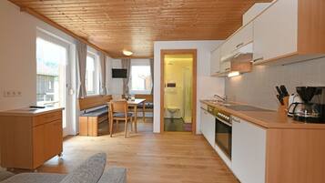 A compact kitchen with wooden cabinets, a dining area with a bench, and a visible bathroom.