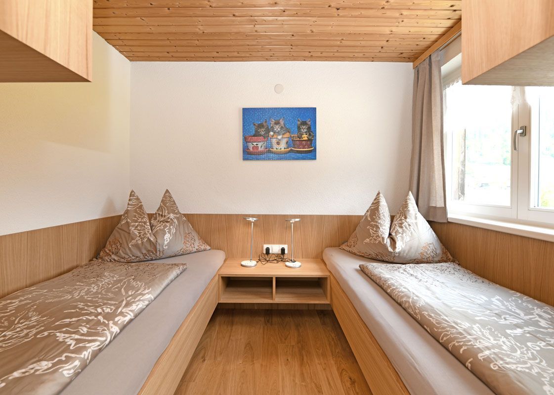 Una habitación con dos camas, una mesita, un cuadro en la pared y una ventana con cortinas.