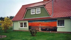 A house with a red-tiled roof, a green exterior wall, and a mural of a sunset on the side. - Sunset apartment (Fuhlendorf)