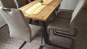 A dining area with a wooden table, four grey upholstered chairs, a small potted plant, and a microwave on the wall. - Sunset apartment (Fuhlendorf)