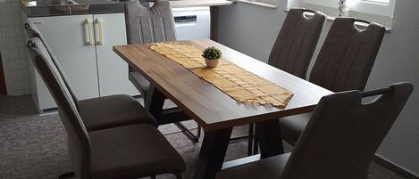 Une cuisine compacte avec des meubles blancs, un four à micro-ondes et une machine à café. On y trouve une table à manger avec quatre chaises et une petite plante en pot.