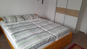 A single bed with striped bedding, a wooden headboard, a nightstand with a lamp, and a wardrobe with a wooden panel design. - Sunset apartment (Fuhlendorf)