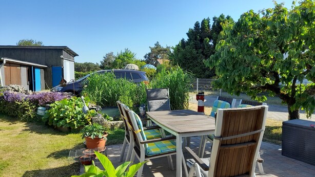 A patio with a table and chairs, surrounded by potted plants and a car. - Sunset apartment (Fuhlendorf)
