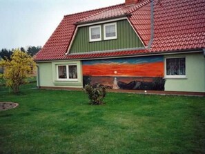 A house with a red-tiled roof, a green exterior wall, and a mural of a sunset on the side. - Sunset apartment (Fuhlendorf)