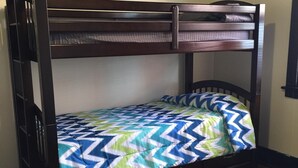 Een stapelbed met een bedspreider met patroon, houten frame en twee lades.
