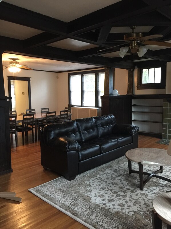 A living room with a black leather sofa, wooden dining table, chairs, and a patterned rug.