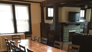 Een eetgedeelte met een houten tafel en stoelen, een keuken met een betegelde achterwand, en een televisie op het aanrecht.
