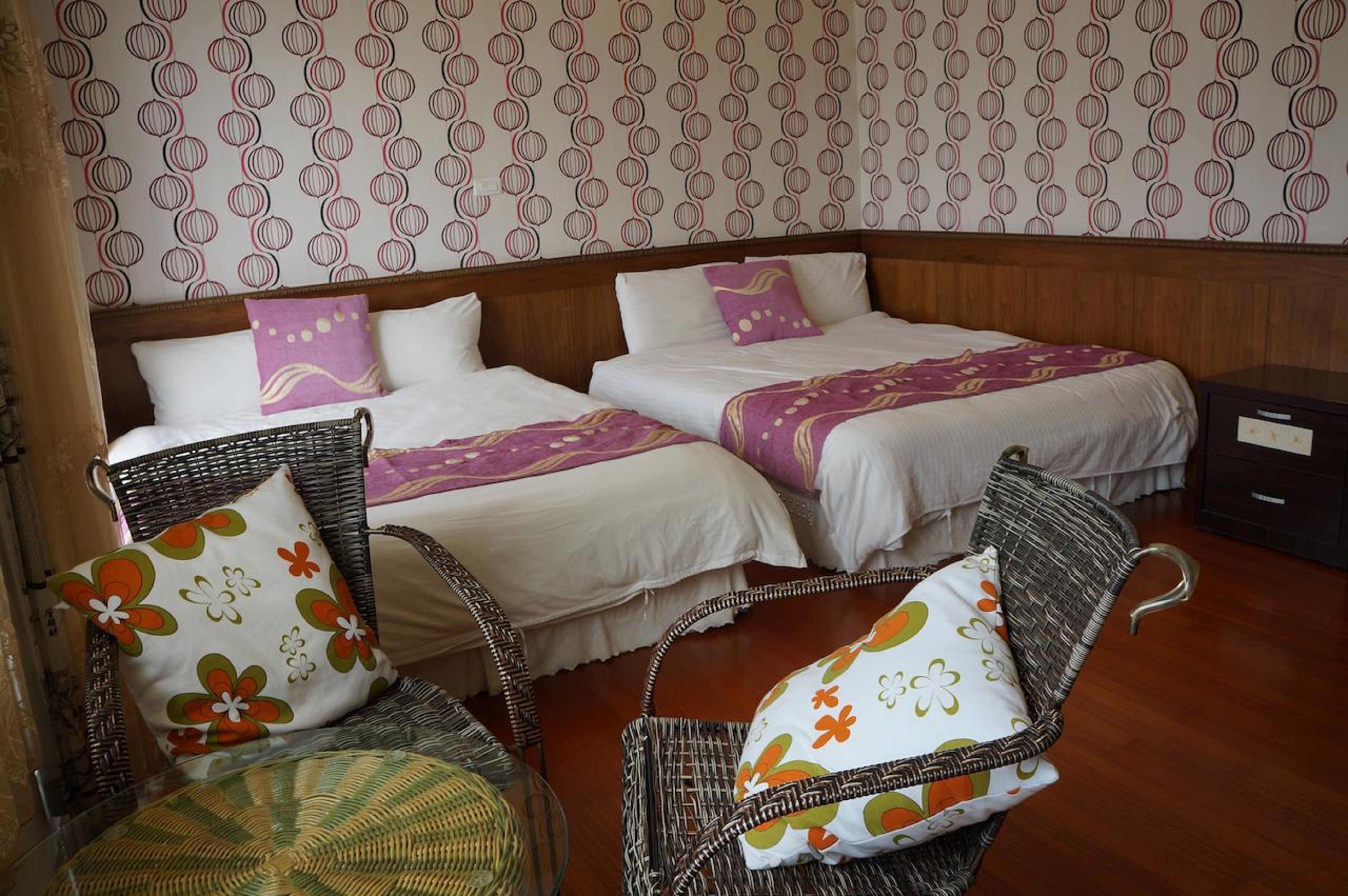 Une chambre d’hôtel avec deux lits, des fauteuils en osier et un papier peint à motifs.