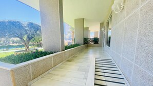 A covered outdoor corridor with a tiled floor, a small set of steps leading to a door, and a view of a landscaped garden with trees and bushes. - A29 - Wonderful urbanization in Cala de Finestrat (Cala de Finestrat)