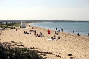 A beach with people sunbathing and swimming, a lifeguard tower, and a clear sky.