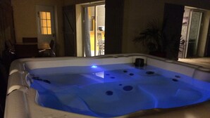 Un jacuzzi con iluminación azul, un banco de madera y una puerta que da a un balcón.