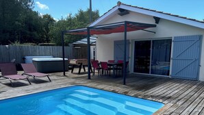 Un patio trasero con piscina, terraza de madera, mobiliario exterior y un área de patio cubierta.