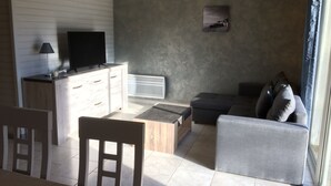 Una sala de estar con una televisión sobre un mueble de madera, un sofá gris, una mesita de madera y un radiador.