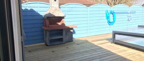 An outdoor patio with a stone-built barbecue grill and a blue fence.
