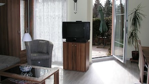 A living room with a television on a wooden cabinet, a chair, a coffee table, and a sliding glass door leading to a patio. - Domizil Neu Venedig (Berlin)
