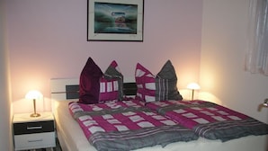 A neatly made bed with a checkered bedspread and pillows, two bedside tables with lamps, a framed picture on the wall, and a striped rug on the floor. - Domizil Neu Venedig (Berlin)