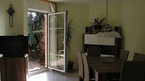 A modern living room with a television, a dining area with a table and chairs, and a sliding glass door leading to a patio. - Domizil Neu Venedig (Berlin)