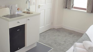 A compact hotel room with a kitchenette, a white door, a window with curtains, and a grey carpet. - Kelpies Serviced Apartments (Falkirk)