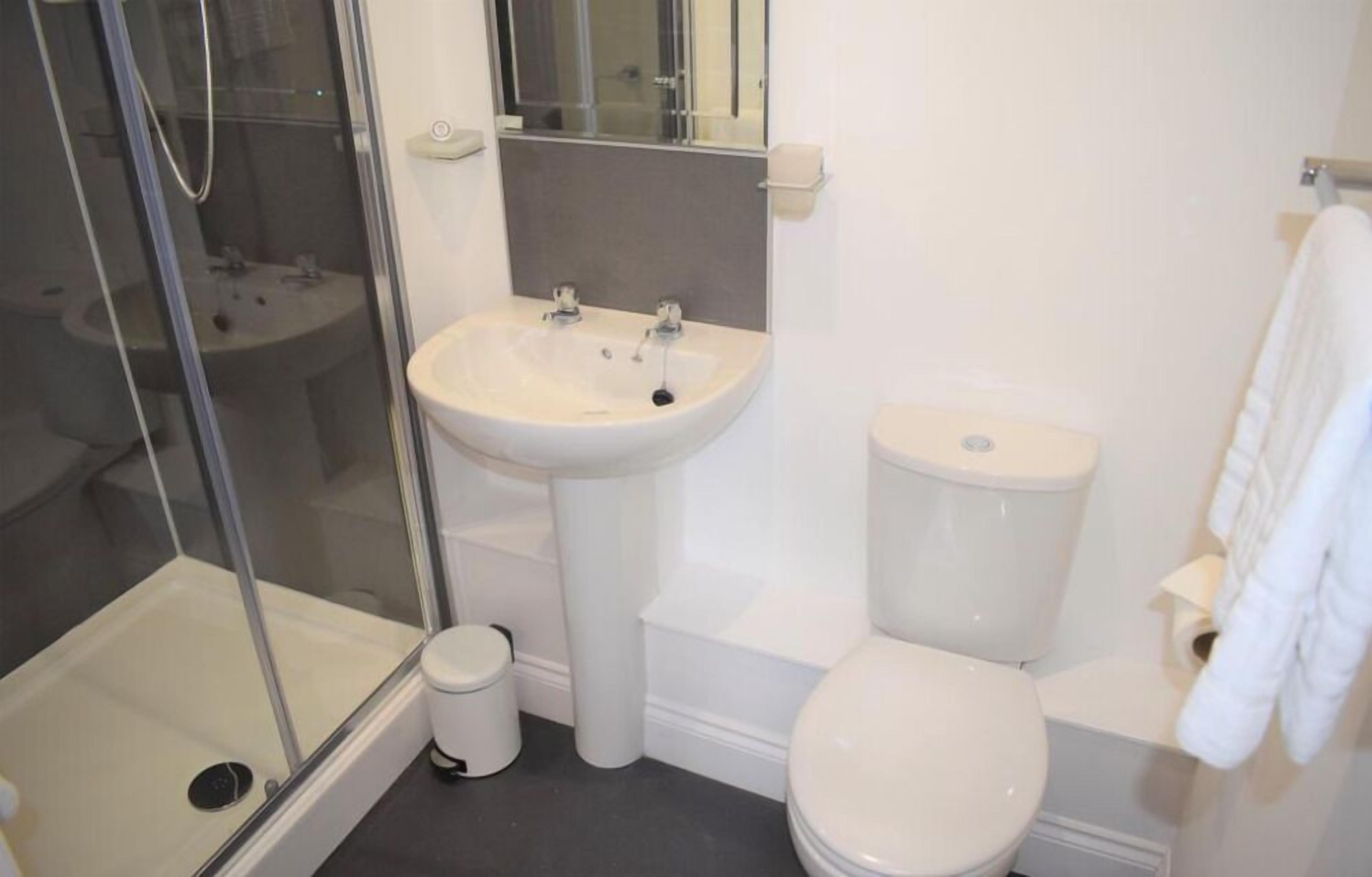 A bathroom with a glass-enclosed shower, a pedestal sink, a toilet, and a towel rack.
