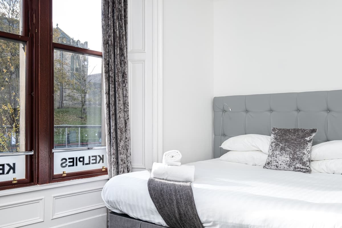 A hotel room with a bed, a window with curtains, and a view of a building outside.