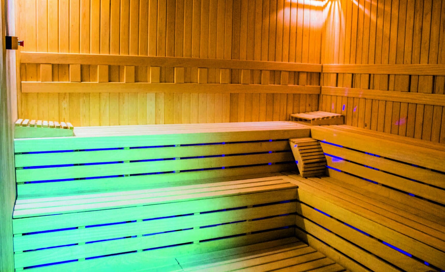 A sauna with wooden benches and steps, illuminated by blue lighting.