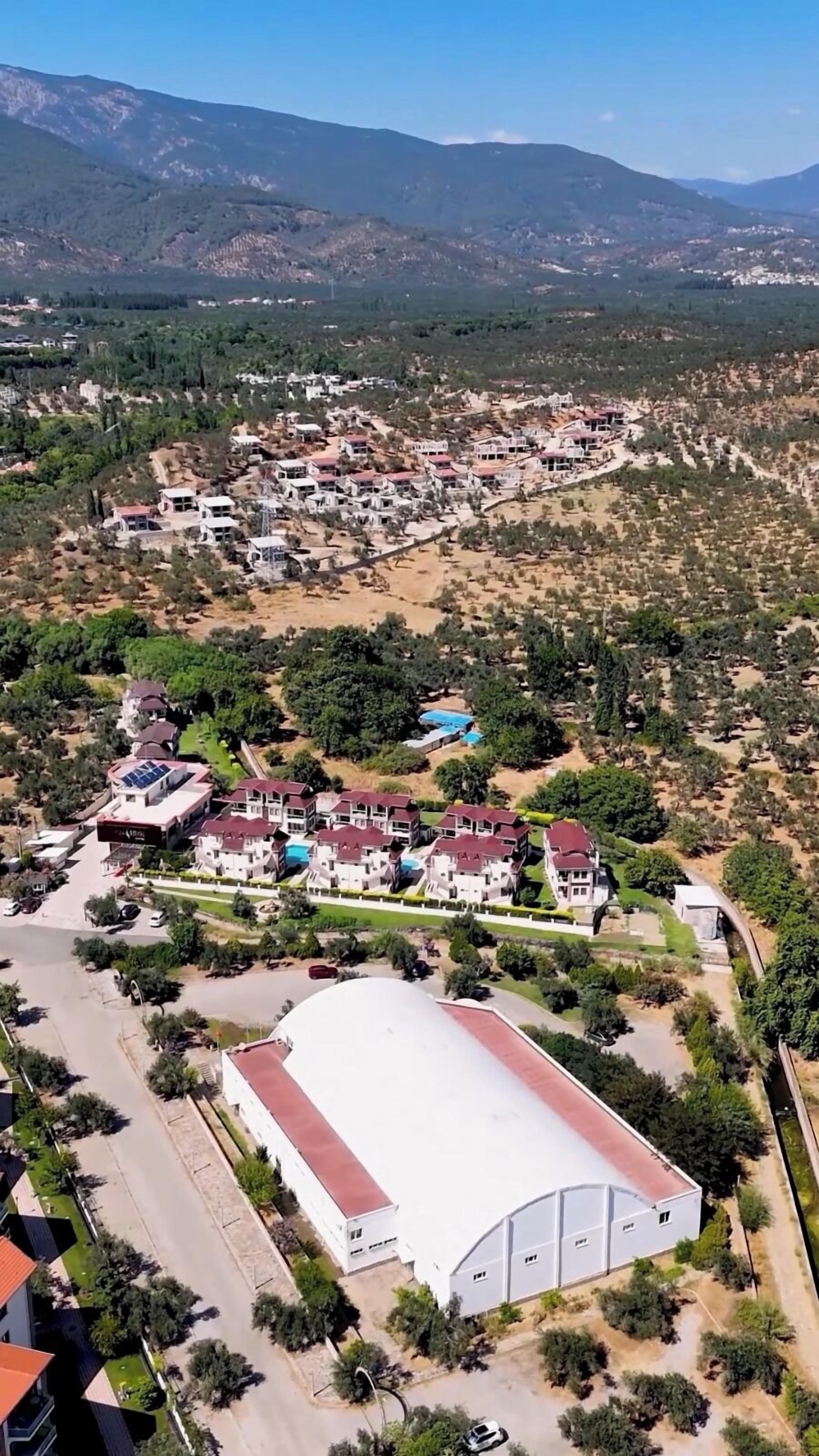 Vista aérea de una zona residencial con casas, un edificio blanco grande y vegetación circundante.