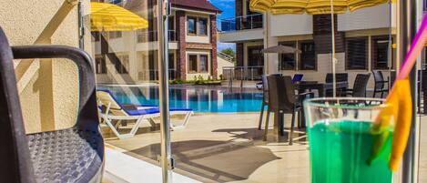 A poolside area with lounge chairs, umbrellas, and a glass table with a drink.
