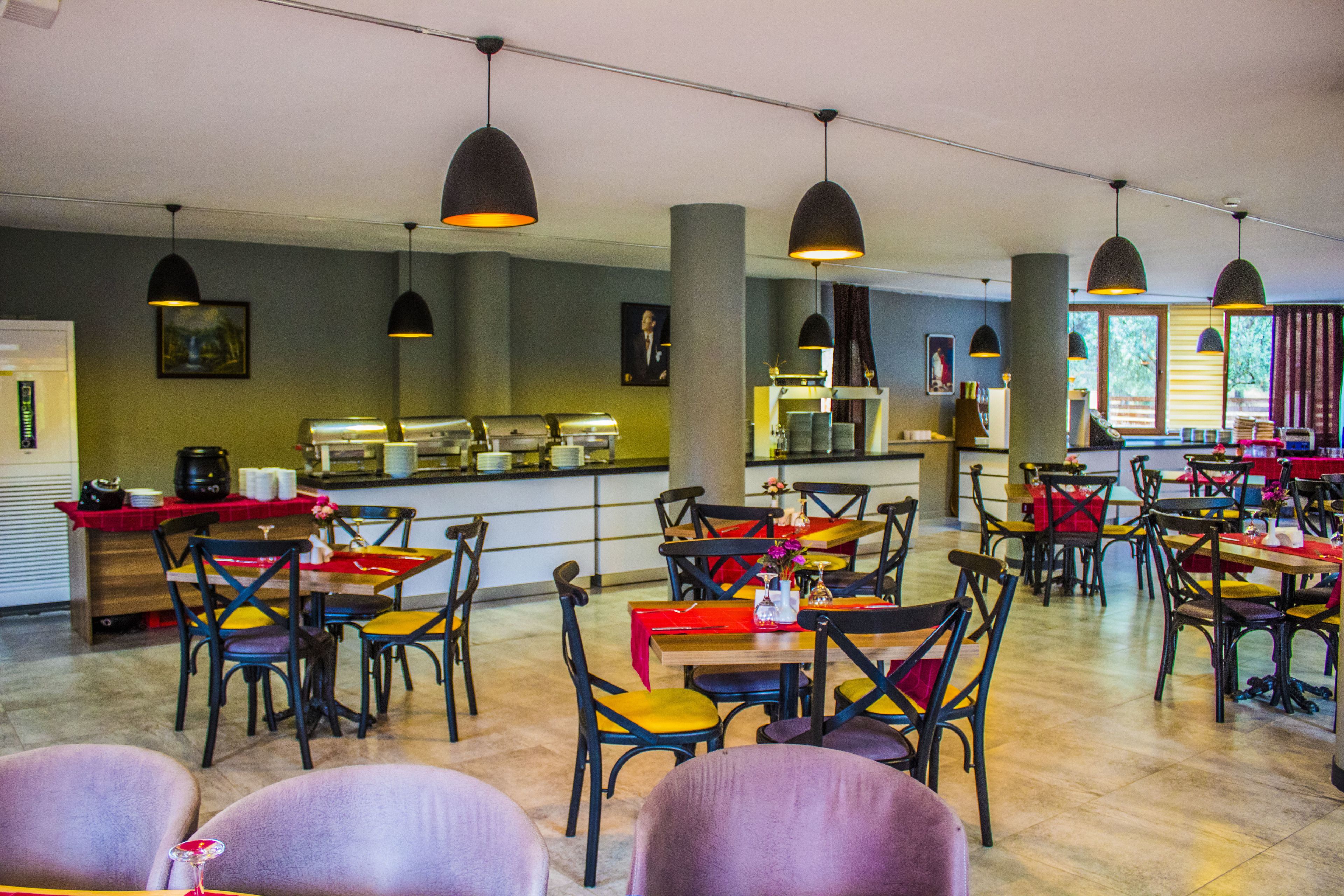 Un restaurante con varias mesas y sillas, iluminación colgante y una zona de cocina al fondo.