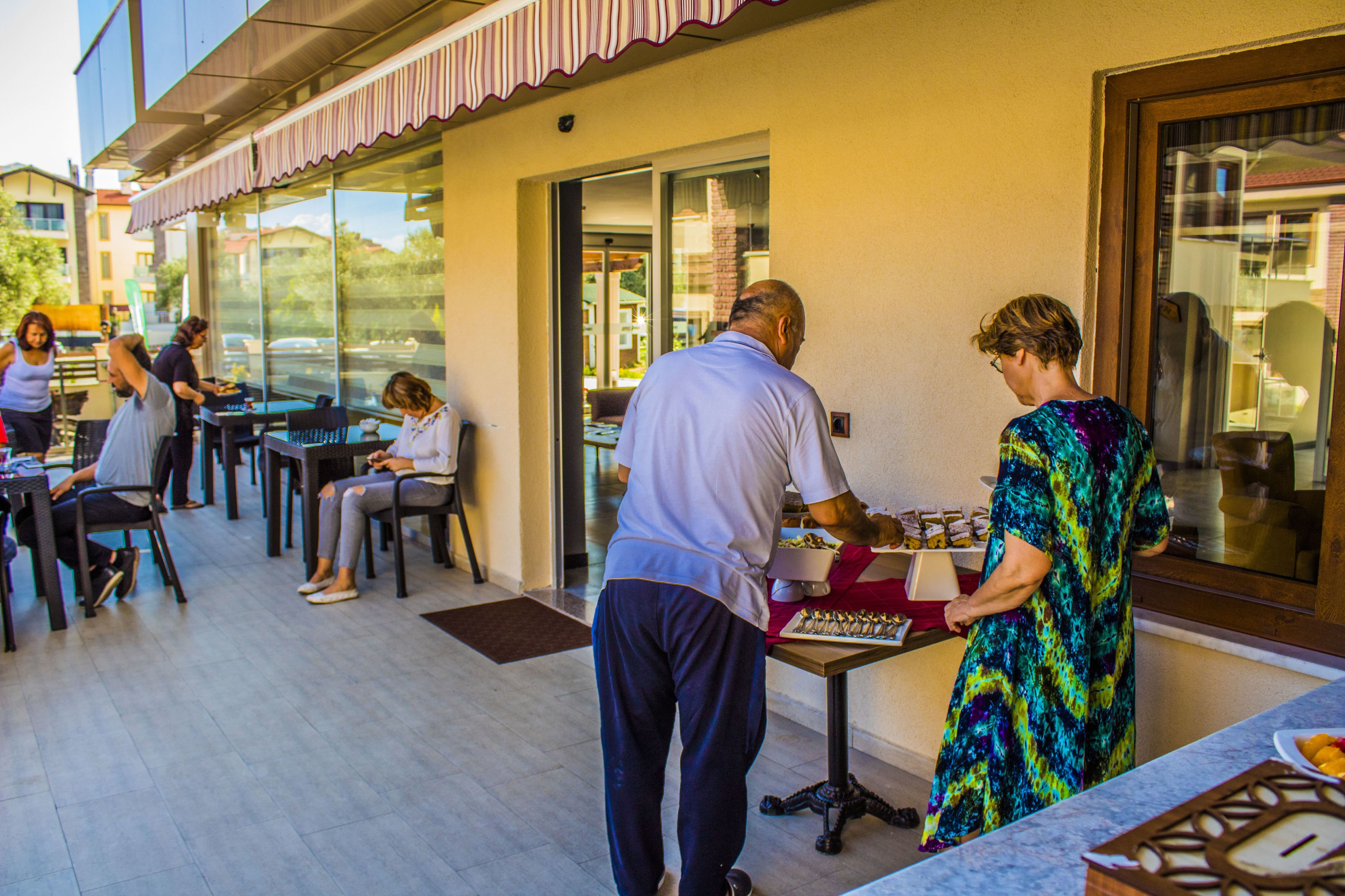 An outdoor dining area with tables and chairs, a counter with food items, and a view of the street and buildings in the background.