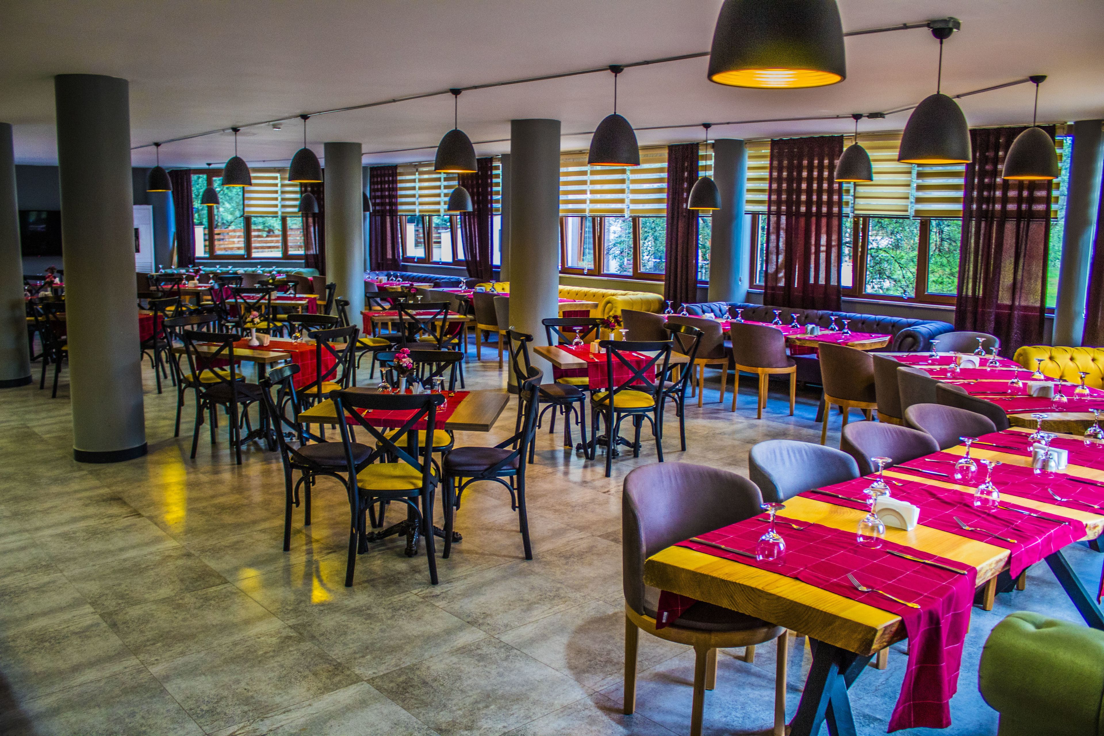 Un restaurante espacioso con varias zonas de comedor, amplias ventanas e iluminación colgante moderna.