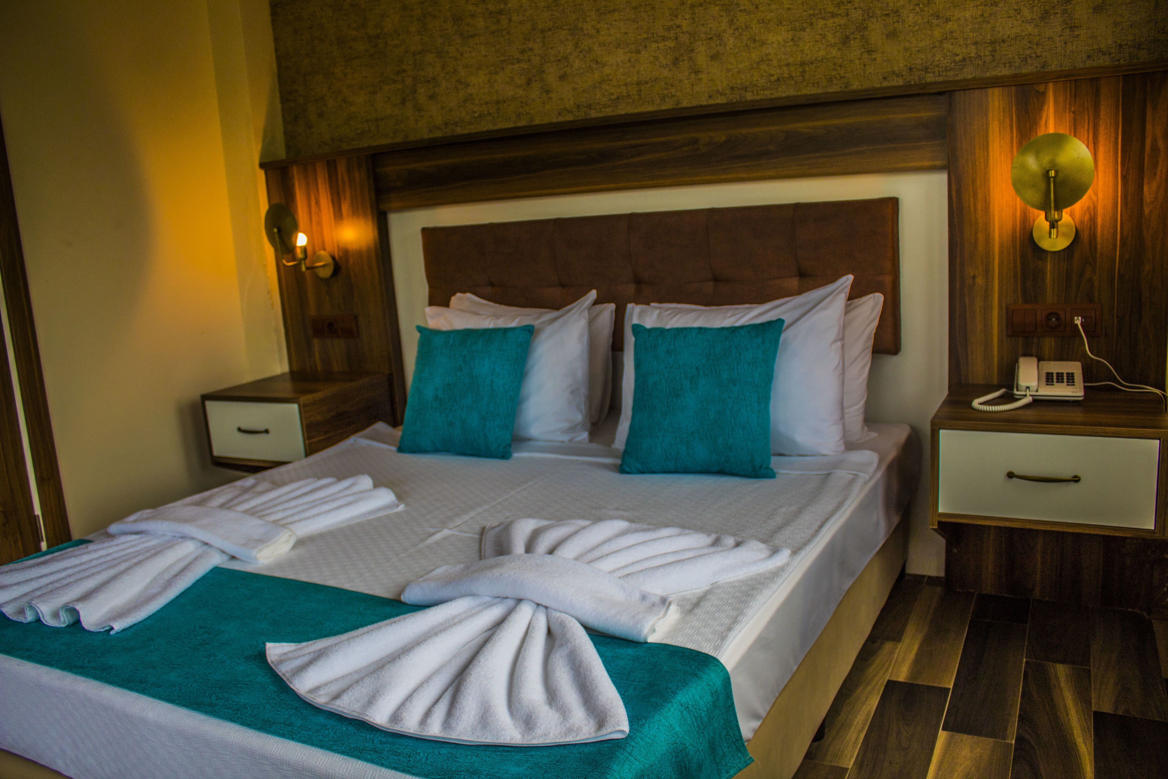 A hotel room with a large bed, two bedside tables, a nightstand, and a wall-mounted lamp.